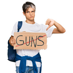 Young hispanic man holding no guns warning banner with angry face, negative sign showing dislike with thumbs down, rejection concept