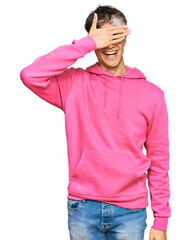 Fototapeta premium Young hispanic man wearing casual pink sweatshirt smiling and laughing with hand on face covering eyes for surprise. blind concept.