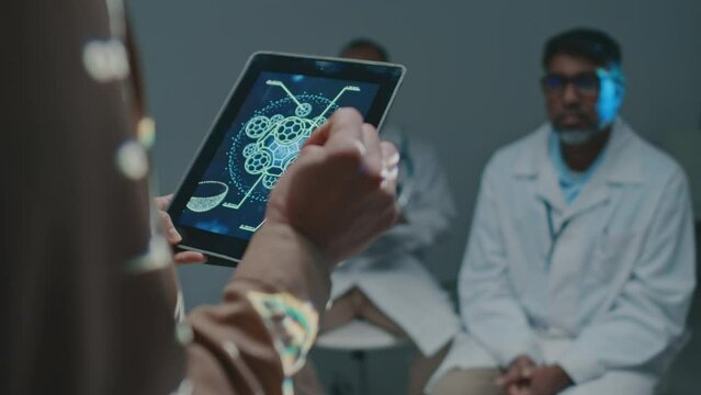 Medium close-up shot of unrecognizable female pharmaceutical sales representative with presentation slide on tablet computer promoting new drug or therapy to doctors at conference