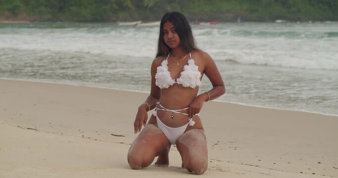 Dressed in a white bikini, an Indian girl embraces the tranquility of a Caribbean beach, its sands as white as snow.