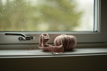 knitting project in pale pink color, seen in a windowsill on a rainy day