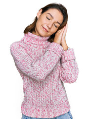 Young caucasian girl wearing wool winter sweater sleeping tired dreaming and posing with hands together while smiling with closed eyes.