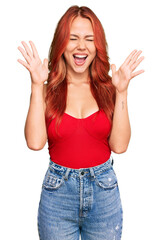 Young redhead woman wearing casual clothes celebrating mad and crazy for success with arms raised...