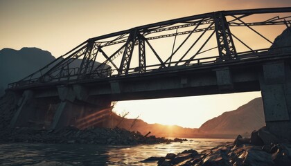 Fototapeta premium A bridge arches over a calm river, bathed in the soft light of dusk with mountains looming in the distance. The setting sun filters through, creating a serene atmosphere around the sturdy structure