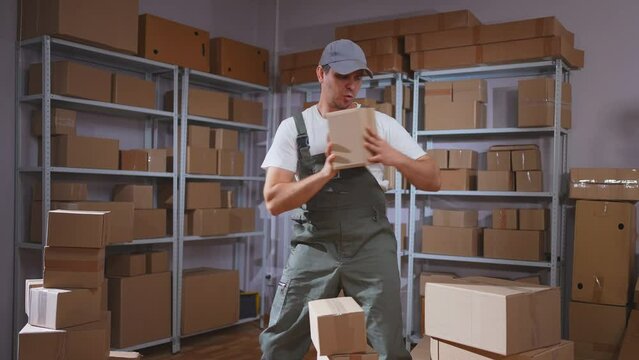 A positive male movers in uniform dancing in a warehouse,folding boxes of parcels