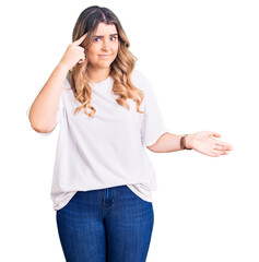 Young caucasian woman wearing casual clothes confused and annoyed with open palm showing copy space and pointing finger to forehead. think about it.