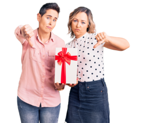 Couple of women holding gift with angry face, negative sign showing dislike with thumbs down, rejection concept