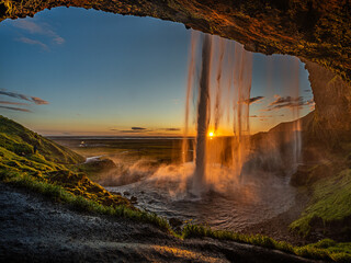 Die Mitternachtssonne scheint durch den Wasserfall Seljalandsfoss, Wasserfall von hinten fotografiert, Höhle hinter Wasserfall sichtbar