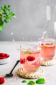 Spritziges Sommer Getr&auml;nk mit Himbeeren in zwei Gl&auml;ser auf einem grauen Tisch. Bewegung, Wassertropfen.
