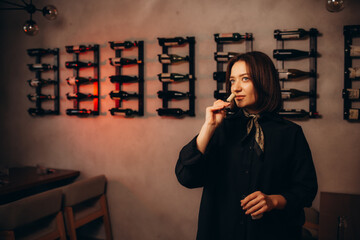 Focused female wine expert smells wine into glass, holding bottle and reads label with...