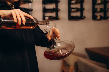 Professional female sommelier pours red wine from decanter to the glass, close up image. Woman...