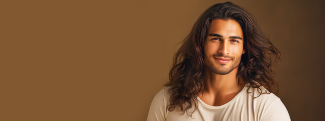 Portrait of an elegant sexy smiling Latino man with perfect skin and long hair, on a beige background.
