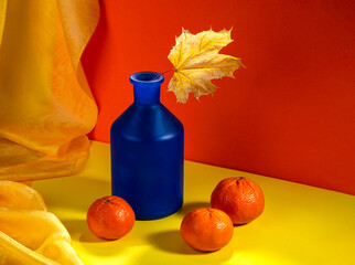 Bright still life with an autumn leaf in a blue bottle on a bright background