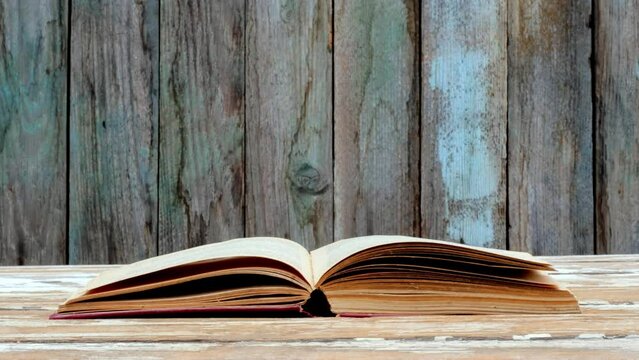 Gusts of wind turn the pages of an open book on an old wooden table 4k video