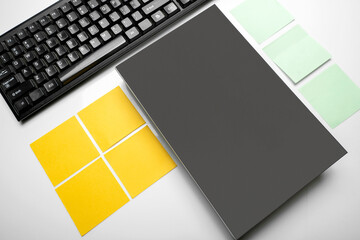 Top view of fffice supplies of computer keyboard, sticky notes and blank black notebook isolated over white background.