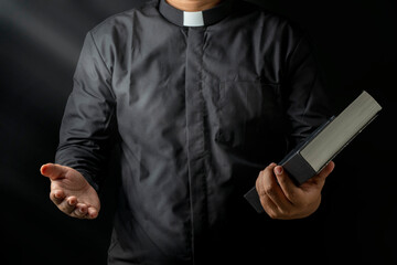 Young priest holding bible and other hand stretching isolated on black background.