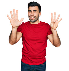 Hispanic man with beard wearing casual red t shirt showing and pointing up with fingers number nine...