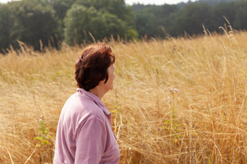 Naklejka na ściany i meble Mature woman standing in the middle of a field of tall grass