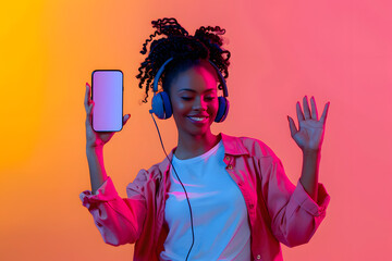 Energetic black lady dancing with headphones, holding smartphone with blank screen, vibrant backdrop - obrazy, fototapety, plakaty