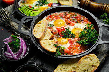Tasty Breakfast Shakshuka in an Iron Pan. Fried eggs with tomatoes. On a black stone background. - obrazy, fototapety, plakaty