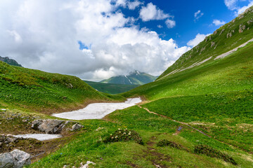 Scenic panoramic view of idyllic rolling hills landscape with blooming meadows and snowcapped alpine mountain peaks in the background on a beautiful sunny day.