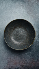 Ceramic dark round textured plate. Close up on gray concrete background. Free space for text. - 774779052