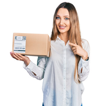 Beautiful caucasian woman holding delivery package smiling happy pointing with hand and finger