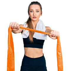 Beautiful caucasian woman training arm resistance with elastic arm bands relaxed with serious expression on face. simple and natural looking at the camera.