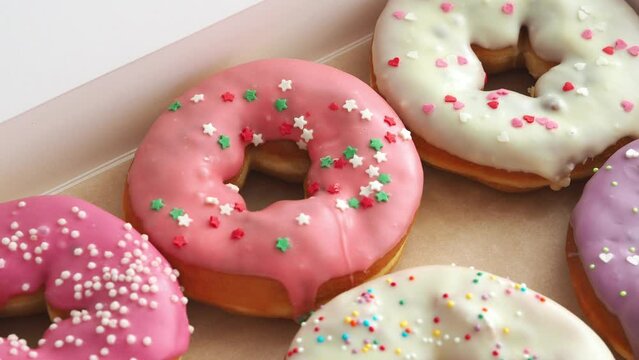 Freshly baked glazed donuts with filling lie in a box. Pink chocolate icing on donuts. Sweet gift in a box. June 7 National Donut Doughnut Day.