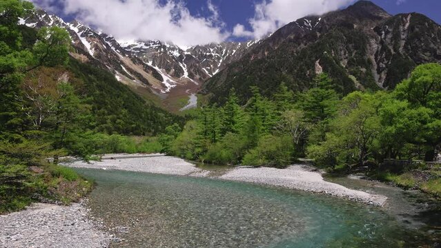 Clear river flowing through forest from snowcapped mountains in the distance