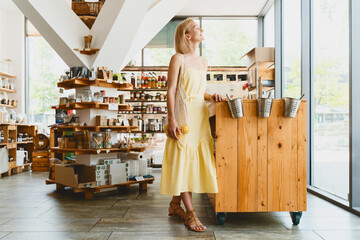Smiling woman buying organic food and eco products in sustainable plastic free store. Happy female customer shopping at local grocery shop.