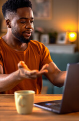 Young African American man sitting at home working while using laptop.