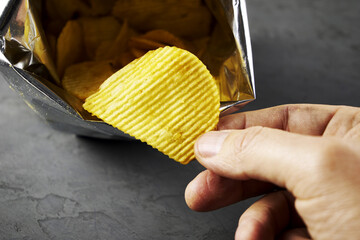 A hand takes potato chips from a pack