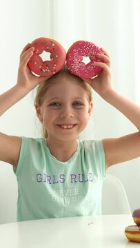 Vertical video. The girl holds 2 donuts in her hands like ears. Funny child with donuts. National Donut Day in the USA. Children's party. Sweet dessert. The image of a cartoon character.