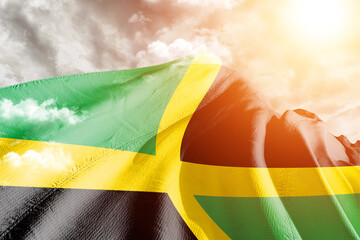 Jamaica national flag cloth fabric waving on beautiful cloudy Background.