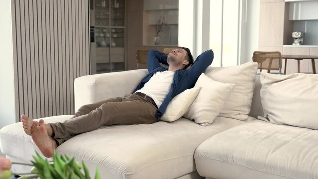 A man lies down on a comfortable sofa in order to relax at home. A satisfied person may feel tired after taking a nap.
