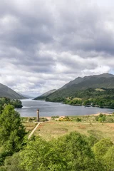 Fototapete Glenfinnan-Viadukt Vertically framed, the Glenfinnan Monument rises beside the serene Loch Shiel, drawing the eye along the water to the distant Scottish Highlands under a broad sky