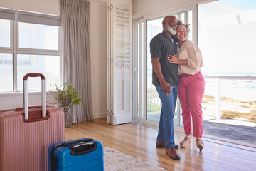 Loving Mature Couple With Luggage Arriving In Beachfront House Overlooking Ocean For Summer Vacation