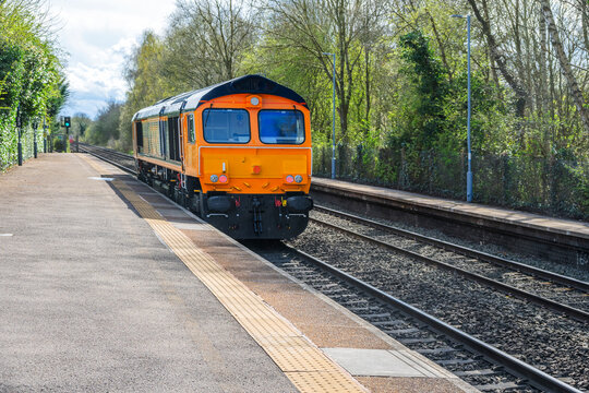 Freight train passing through English rural country passenger commuter station, West Midlands England UK.