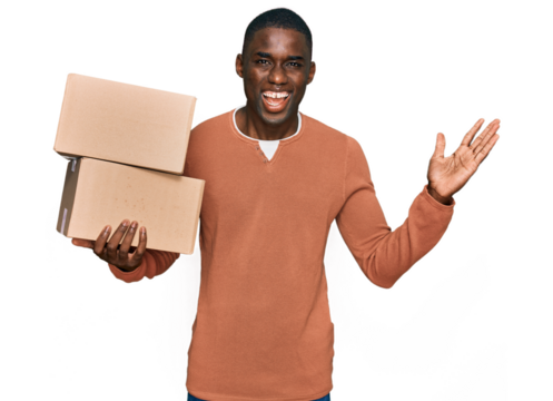 Young african american man holding delivery package celebrating victory with happy smile and winner expression with raised hands