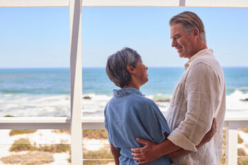 Loving Mature Couple Hugging In Beachfront House Overlooking Ocean For Summer Vacation
