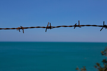 barbed wire against a tranquil blue sea horizon