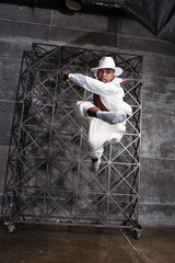Energetic African American male dancer jumps and twirls in a studio wearing white attire, executing pirouettes with grace. Black man dancing indoors © Anna Zhukkova