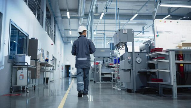 CNC Milling Factory: Confident Asian Male Walking Next to Manufacturing Machines and Using Laptop Computer. Industrial Engineer Monitoring Workflow, Carrying Out Quality Control Operations. Backview