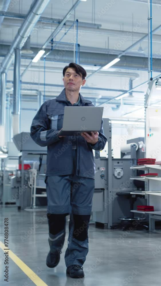 Poster Vertical Screen: Asian Engineer Using a Laptop Computer on the Go at Electronics Manufacturing Factory. Adult Technician Working on Daily Tasks and Analyzing New Production Plans