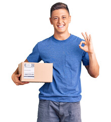Young handsome hispanic man holding delivery package doing ok sign with fingers, smiling friendly...