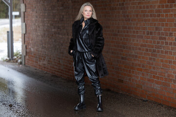 Fototapeta na wymiar Portrait of a beautiful young blonde woman in a black coat on a brick wall background