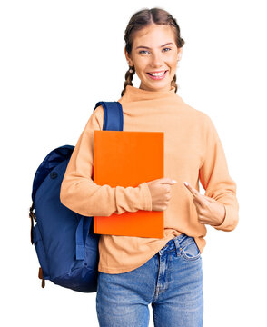Beautiful caucasian woman with blonde hair wearing student backpack and holding book smiling happy pointing with hand and finger