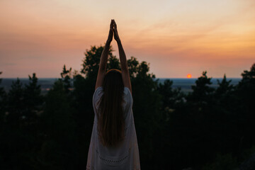 The concept of recreation and unity with nature. A young woman meditates in the mountains against the background of the setting sun.