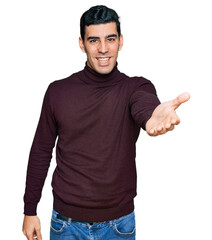 Handsome hispanic man wearing casual turtleneck sweater smiling friendly offering handshake as greeting and welcoming. successful business.